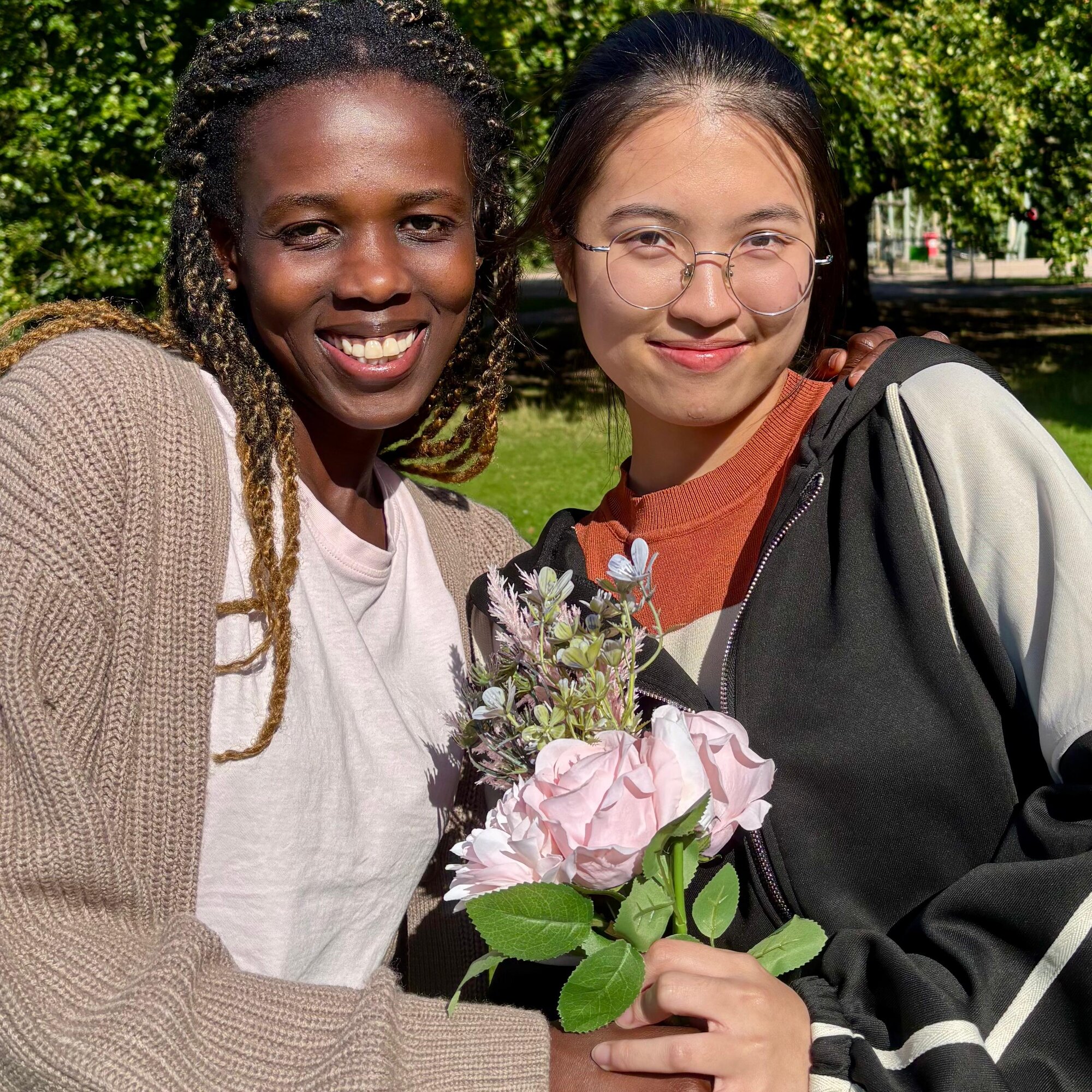 zwei junge Frauen halten gemeinsam einen Blumenstrauß und lächeln in die Kamera